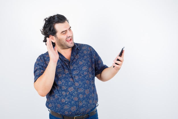 Mature man making video call on mobile phone in shirt and looking cheerful. front view.