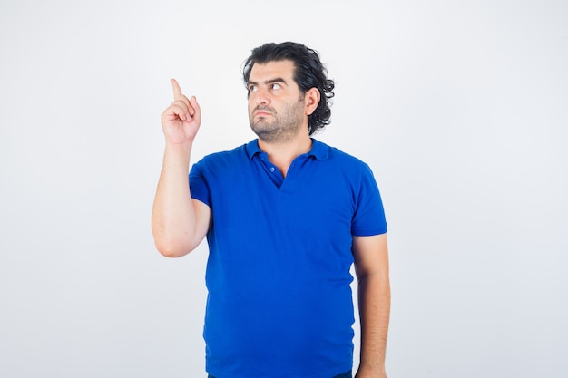 Mature man pointing left with index finger in blue t-shirt, looking focused. front view.