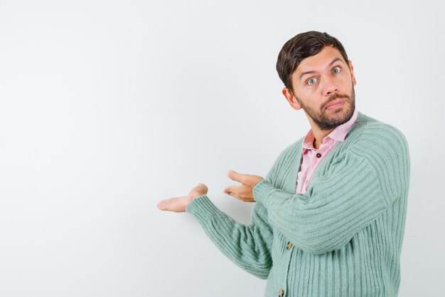 Mature man pretending to show something in shirt, cardigan and looking bewildered. front view.