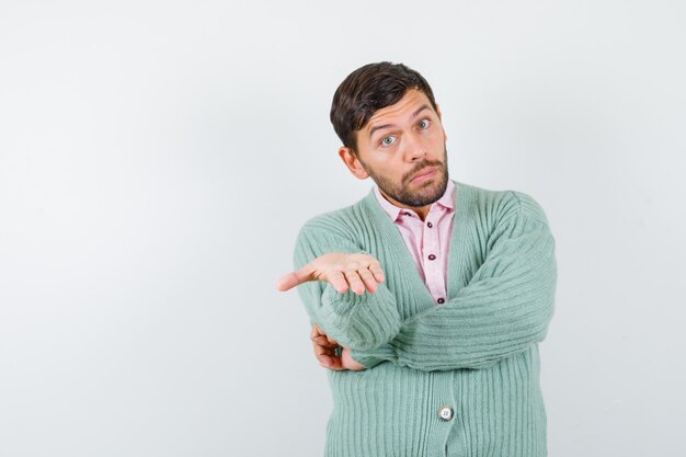 Mature man in shirt, cardigan pretending to hold something and looking surprised , front view.