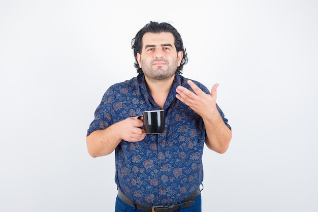 Mature man in shirt holding cup while smelling tea and looking delighted , front view.