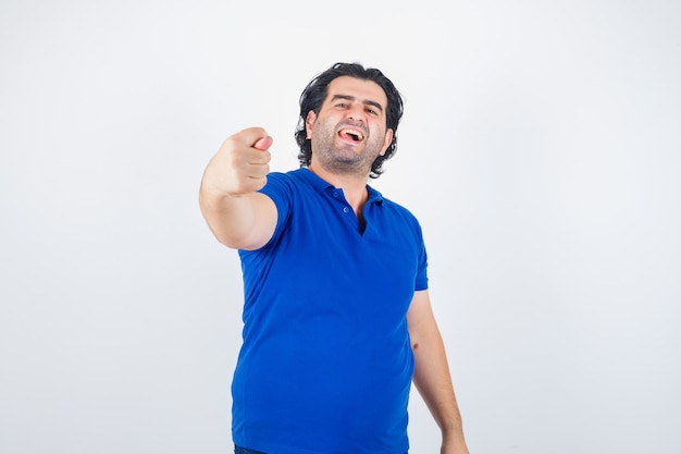 Mature man showing fig gesture in blue t-shirt, looking angry. front view.