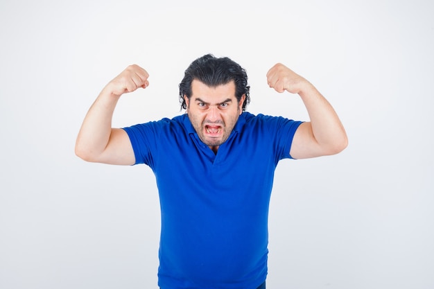 Mature man showing muscles in blue t-shirt, jeans and looking angry