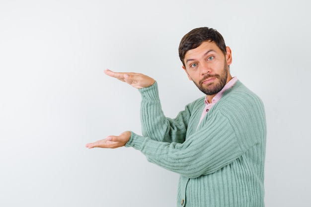 Mature man showing size sign in shirt, cardigan and looking cheerful. front view.