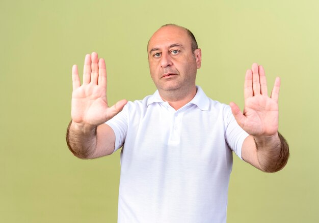 mature man showing stop gesture isolated on olive green