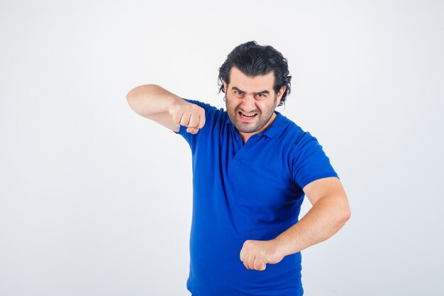 Mature man standing in fight pose in blue t-shirt, jeans and looking confident