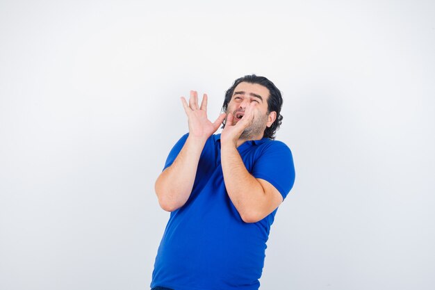 Mature man stretching hands as holding something in blue t-shirt, looking frightened, front view.