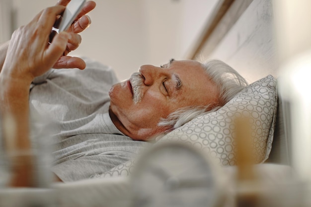 Mature man texting on smart phone while lying down in bed