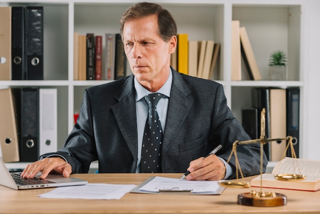 Mature man using laptop while checking the document paper in the courtroom