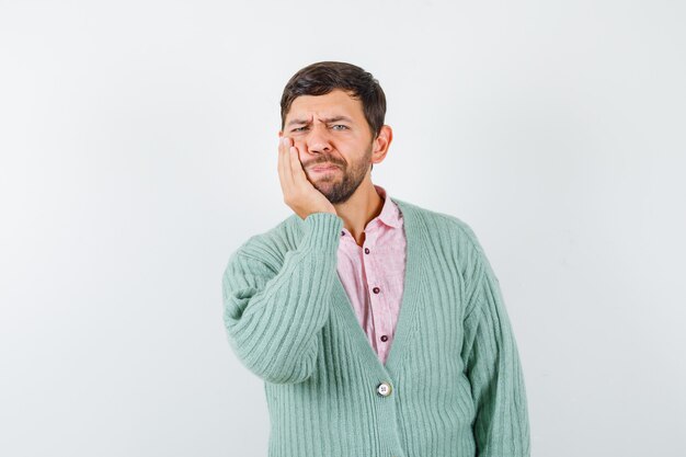 Mature man with hand on blown cheek in shirt, cardigan and looking pensive. front view.