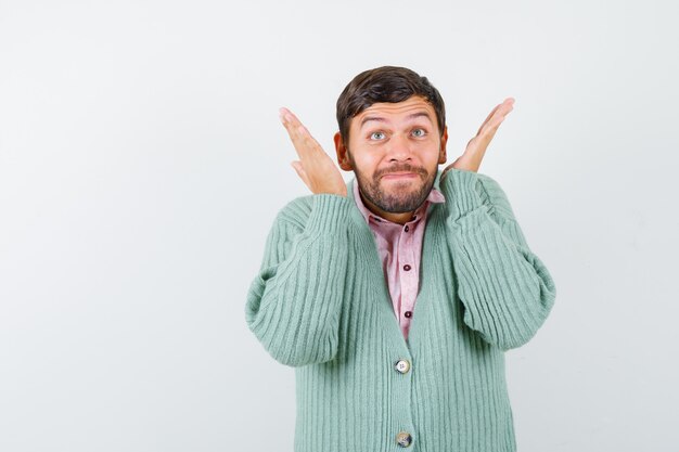 Mature man with hands near face, looking up in shirt, cardigan and looking hopeful , front view.