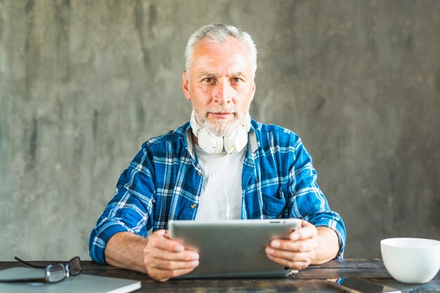 Зрелый человек с наушниками на шее с цифровой планшет