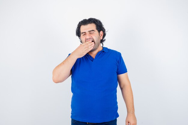 Mature man yawning in blue t-shirt and looking sleepy. front view.