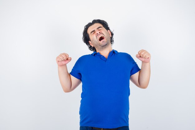 Mature man yawning and stretching in blue t-shirt and looking sleepy. front view.