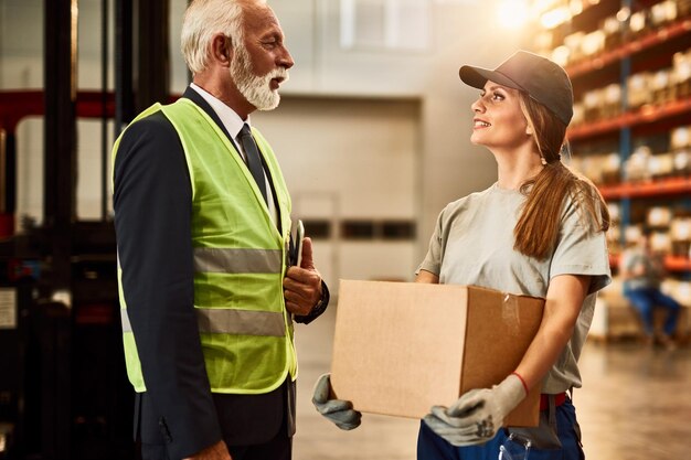 Mature manager communicating with female distribution warehouse worker in industrial building