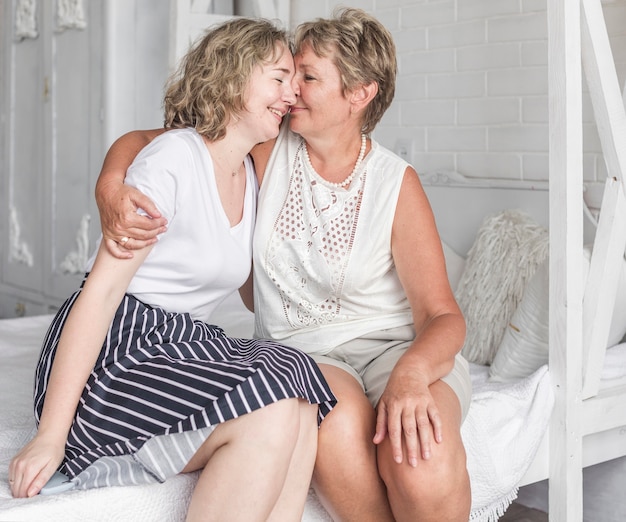 Пожилая мать целует дочь сидя на кровати