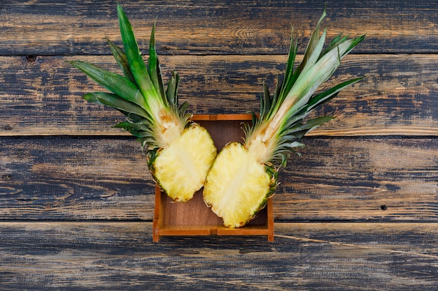 Mature pineapple cut in a half in a wood plate on old wood grunge, top view.