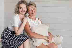 Free photo mature smiling mother holding cushion sitting with her beautiful daughter