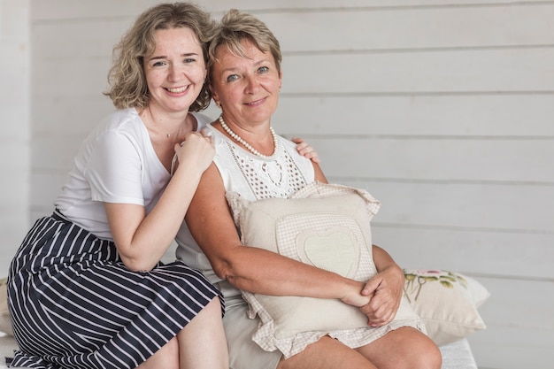 Mature smiling mother holding cushion sitting with her beautiful daughter