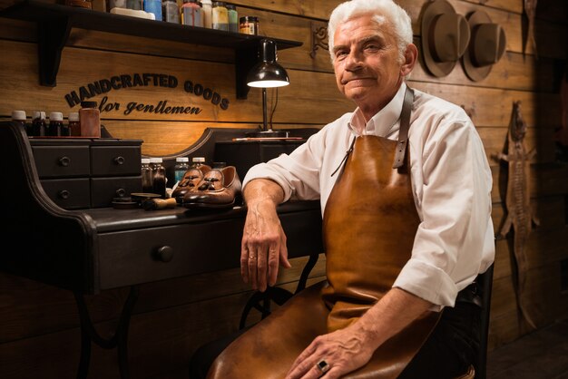 Mature smiling shoemaker in workshop making shoes