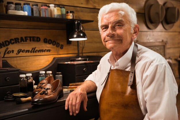 Mature smiling shoemaker in workshop making shoes