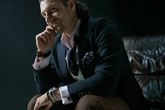 The mature stylish man in a suit on a gray. Businessman sitting on an armchair