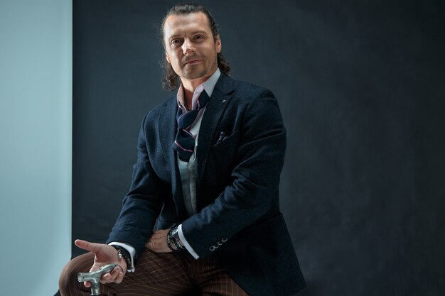 The mature stylish man in a suit on a gray studio background. Businessman sitting on an armchair