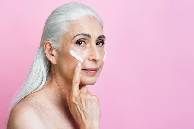 Mature woman applying cream on her face