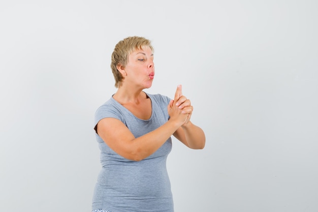 Mature woman blowing on finger pistol in grey t-shirt and looking confident