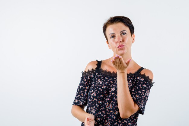 Mature woman blowing kiss in floral blouse, black skirt and looking charming. front view.