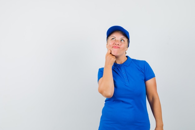 Mature woman in blue t-shirt looking up and looking pensive.