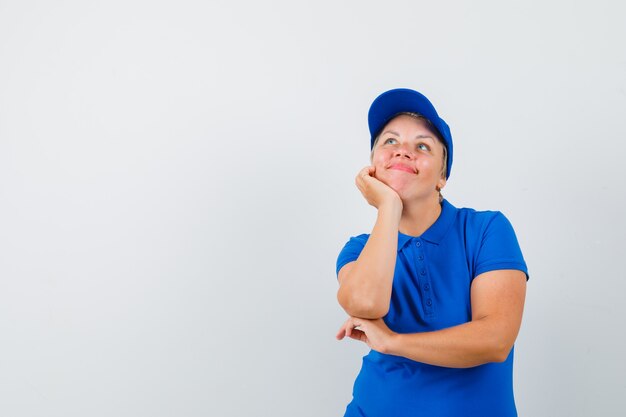 Mature woman in blue t-shirt propping chin on hand and looking dreamy.