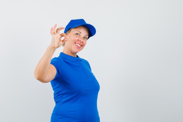 Зрелая женщина в голубой футболке показывает хорошо жест и выглядит весело.