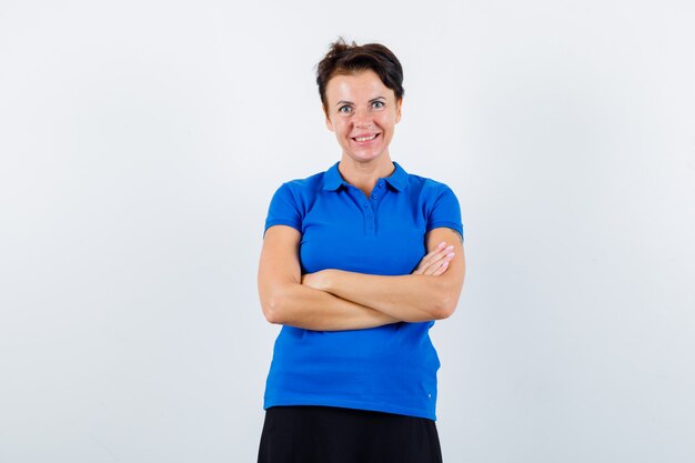 Mature woman in blue t-shirt standing with crossed arms and looking confident , front view.