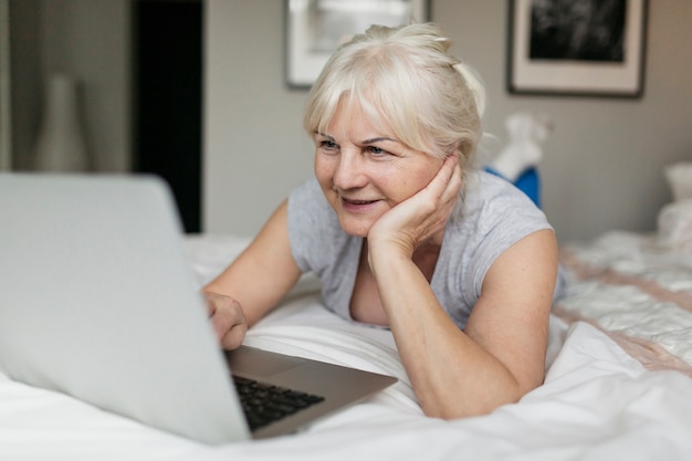 Mature woman browsing laptop in bedroom