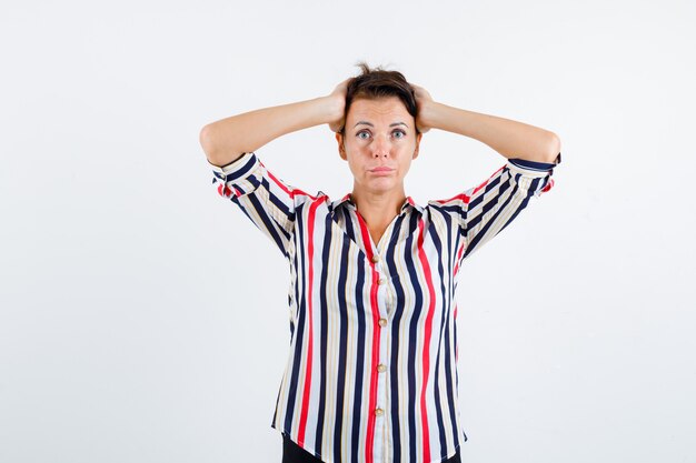 Mature woman clasping head with hands in striped blouse and looking serious. front view.