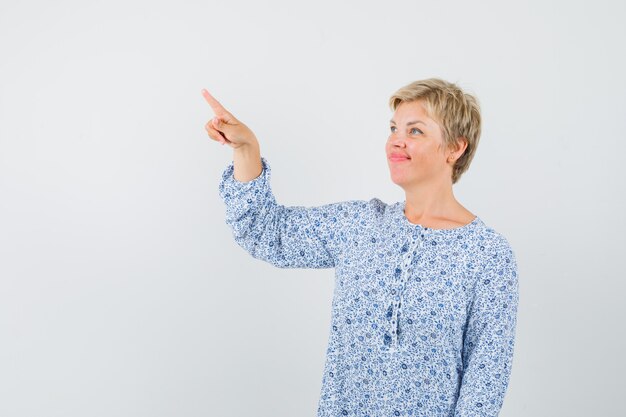 Mature woman in dress pointing at upper left corner and looking focused