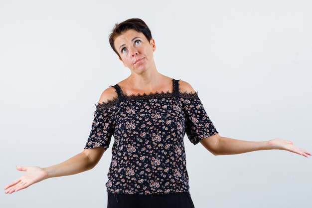 Free photo mature woman in floral blouse, black skirt showing helpless gesture and looking baffled , front view.