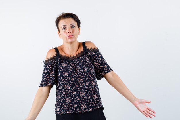 Free photo mature woman in floral blouse, black skirt showing helpless gesture and looking baffled , front view.