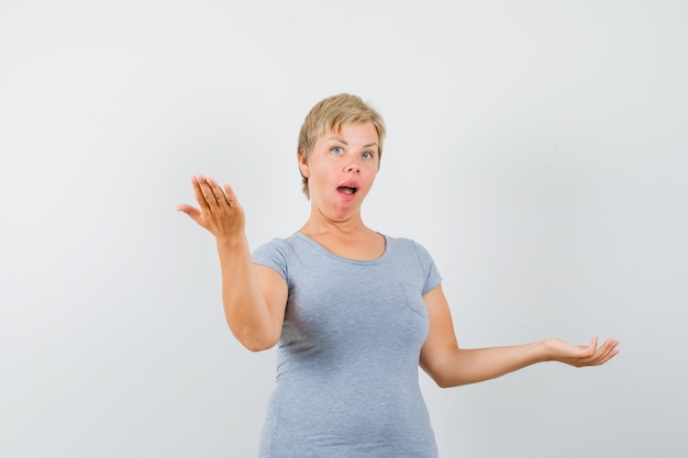 Mature woman in grey t-shirt making scales gesture and looking surprised