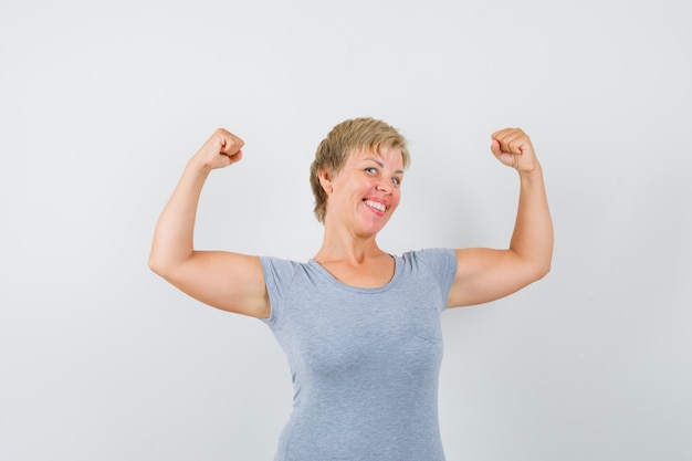 Mature woman in grey t-shirt showing muscles of arms and looking strong