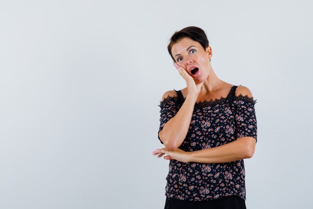 Mature woman holding hand on cheek in blouse and looking puzzled. front view.