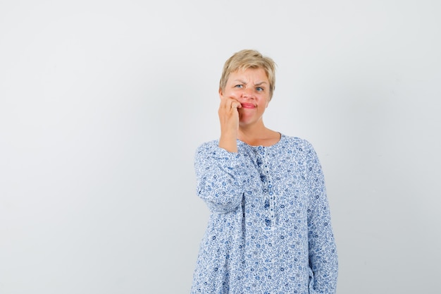 Free photo mature woman holding hand on cheek in dress and looking pensive