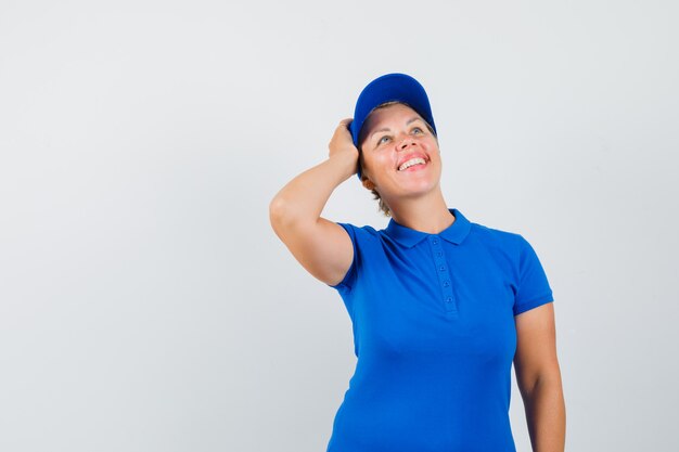 Mature woman holding hand on head in blue t-shirt and looking dreamy.