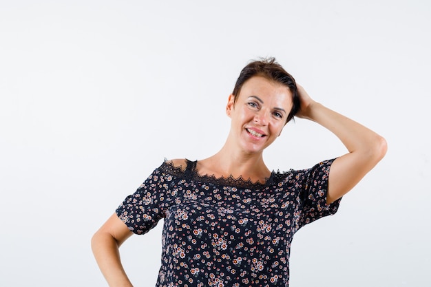 Mature woman holding hand on head in floral blouse, black skirt and looking charming. front view.