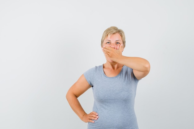 Mature woman holding hand on mouth in grey t-shirt and looking mysterious