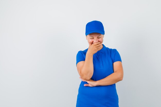 Mature woman holding hand on mouth while laughing in blue t-shirt