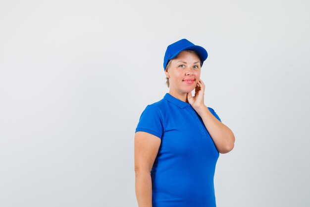 Mature woman holding hand touching cheek in blue t-shirt and looking cute