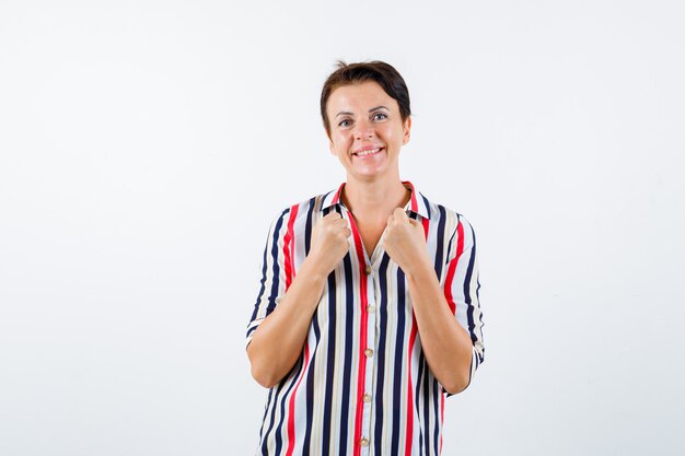 Mature woman holding hands on collars of blouse in striped blouse and looking buoyant. front view.