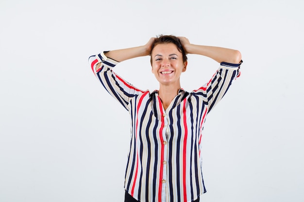 Mature woman holding hands on head in striped blouse and looking buoyant , front view.